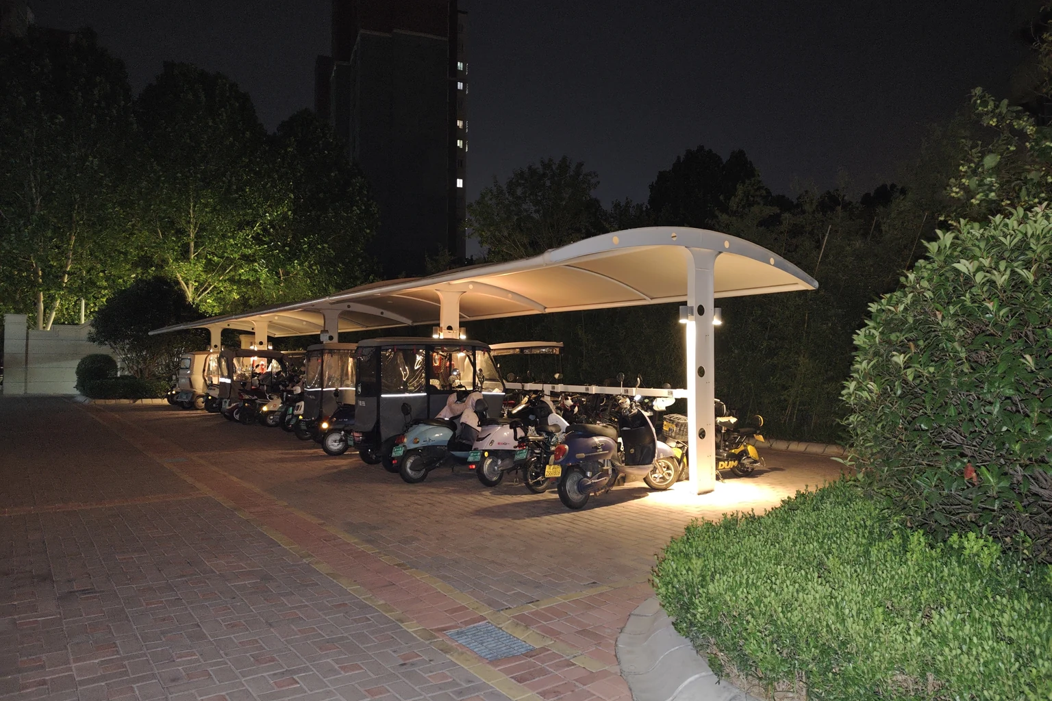 膜结构电动车充电棚夜景实拍，可见停放车辆和横梁上的充电插座