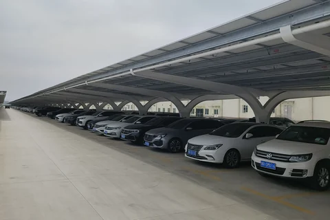 实拍光伏车棚,成排白色弧形钢梁支撑组件屋面,棚下停放车辆