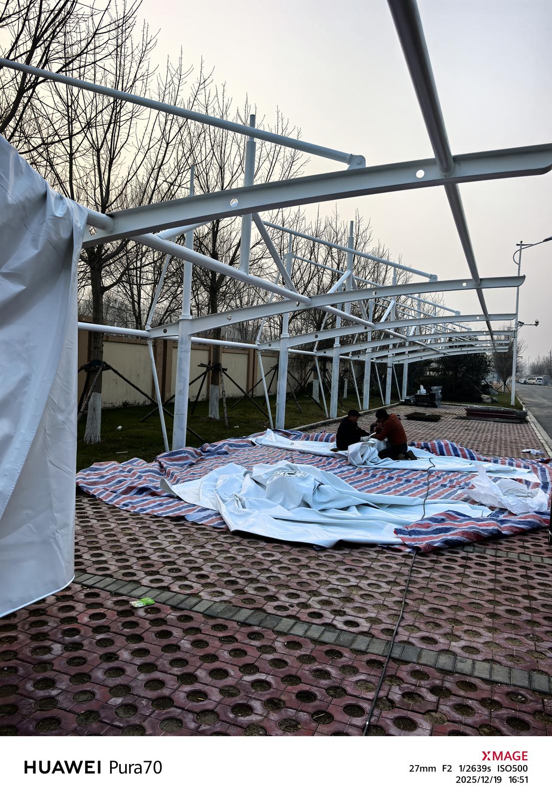 冒顶式车棚骨架下正在展开的白色膜材