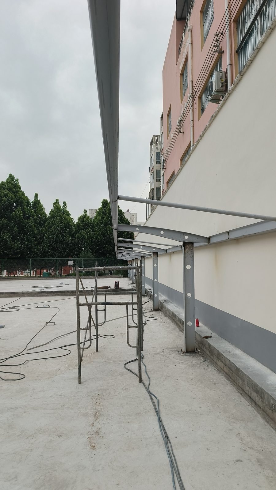 Repeated perforated-column steel frames for a membrane carport beside a building in Xinmi