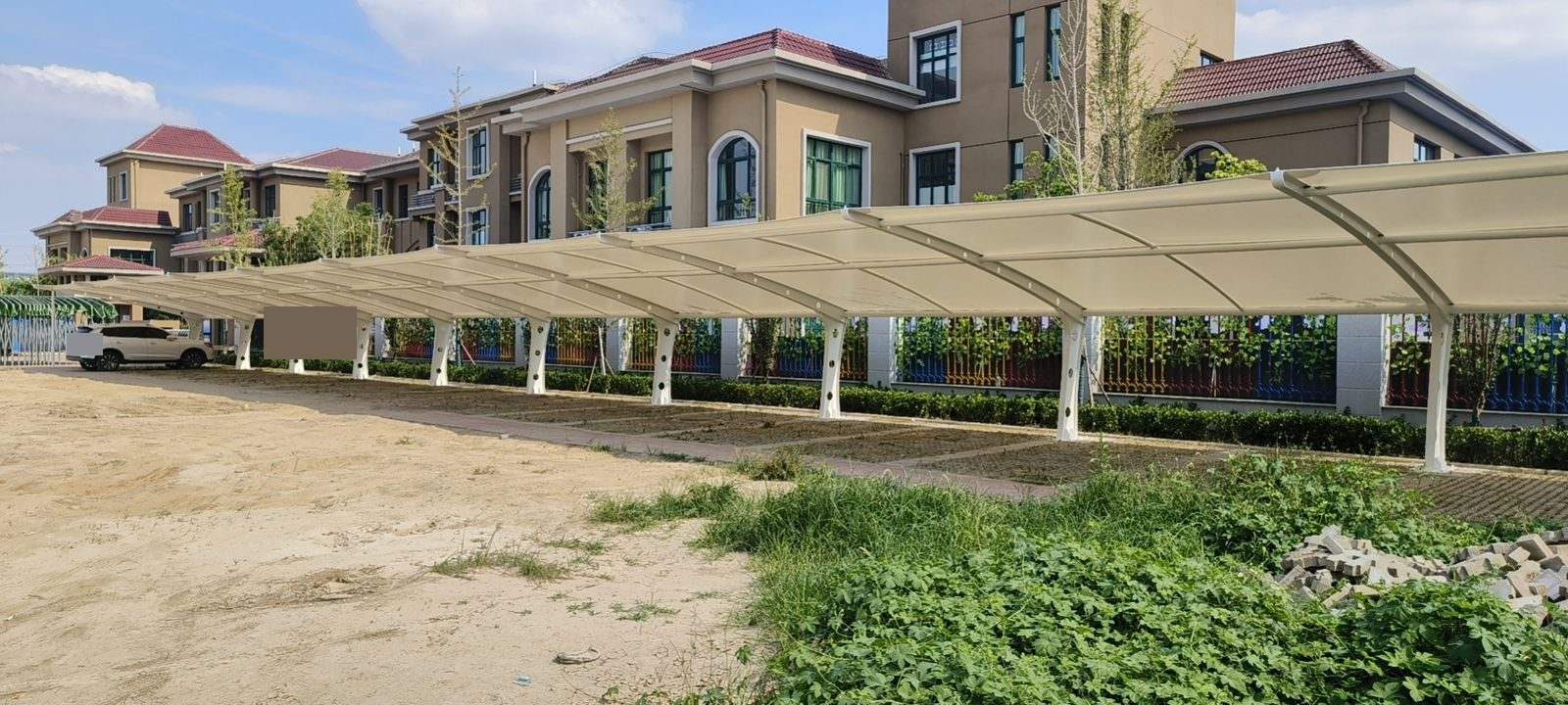 幼儿园围栏旁连续布置的白色膜结构停车棚